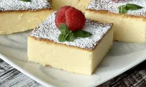 Kremowy i pyszny sernik z mlekiem w proszku, posypany cukrem pudrem i ozdobiony maliną i miętą. Idealny deser!