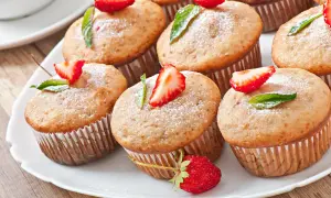 Słodkie muffinki z truskawkami i listkami mięty, oprószone cukrem pudrem, wyglądają jakby były polane polewą z serka mascarpone.