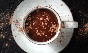 Gorące kakao, posypane pudrem kakaowym, na talerzyku. Czy kakao pobudza? Ten napój z pewnością poprawia nastrój.