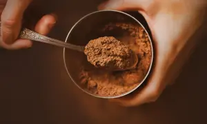 Łyżeczka z kakao nad słoikiem. Zastanawiasz się, ile kcal ma kakao? To zdrowy dodatek do napojów i deserów.