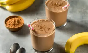 Dwa szklanki koktajlu czekoladowo-bananowego, obok banany i miseczka kakao.