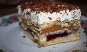 Pyszny porzeczkowiec na herbatnikach z kremem i polewą czekoladową, podany na talerzyku z kwiatowym wzorem.