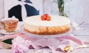 Pyszny sernik nowojorski z mascarpone, ozdobiony truskawkami, na talerzu, obok filiżanki herbaty i piwonii.