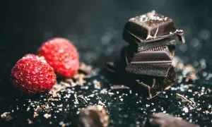 Kawałki ciemnej belgijskiej czekolady w tabliczkach, posypane solą, obok świeżych malin.