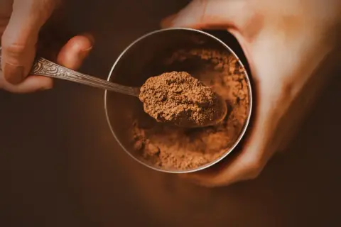Łyżeczka z kakao nad słoikiem. Zastanawiasz się, ile kcal ma kakao? To zdrowy dodatek do napojów i deserów.
