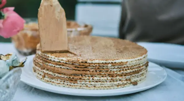 Nakładanie kremu na ciasto na gofrach bez pieczenia. Warstwy wafli przełożone pysznym, karmelowym nadzieniem.