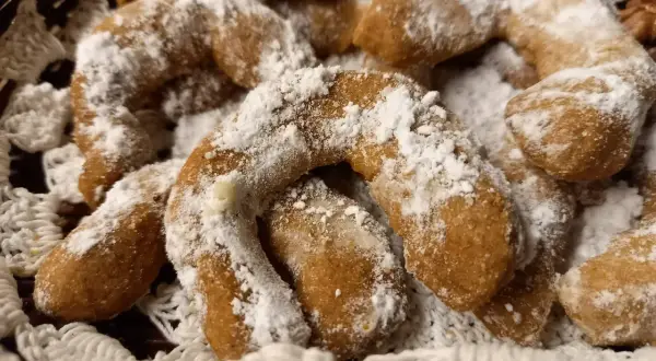 Pyszne ciasteczka orzechowe księżyce, posypane cukrem pudrem, leżą w koszyku wyłożonym koronką.