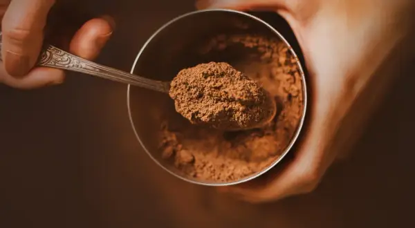Łyżeczka z kakao nad słoikiem. Zastanawiasz się, ile kcal ma kakao? To zdrowy dodatek do napojów i deserów.