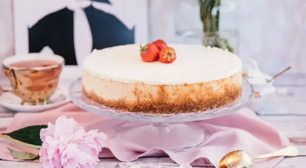Pyszny sernik nowojorski z mascarpone, ozdobiony truskawkami, na talerzu, obok filiżanki herbaty i piwonii.
