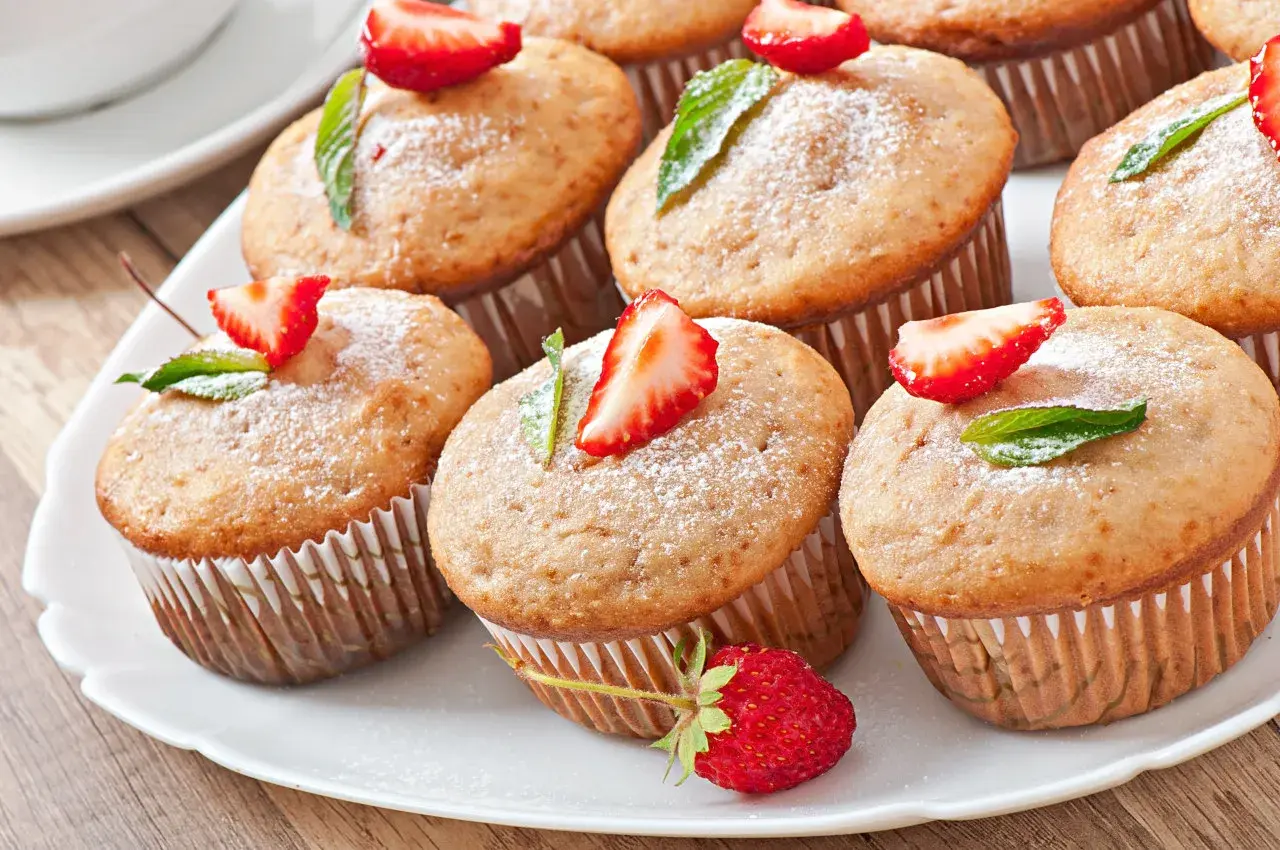 Słodkie muffinki z truskawkami i listkami mięty, oprószone cukrem pudrem, wyglądają jakby były polane polewą z serka mascarpone.