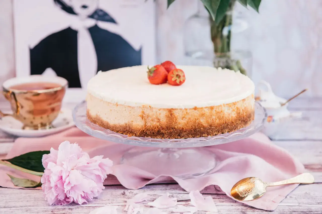 Pyszny sernik nowojorski z mascarpone, ozdobiony truskawkami, na talerzu, obok filiżanki herbaty i piwonii.