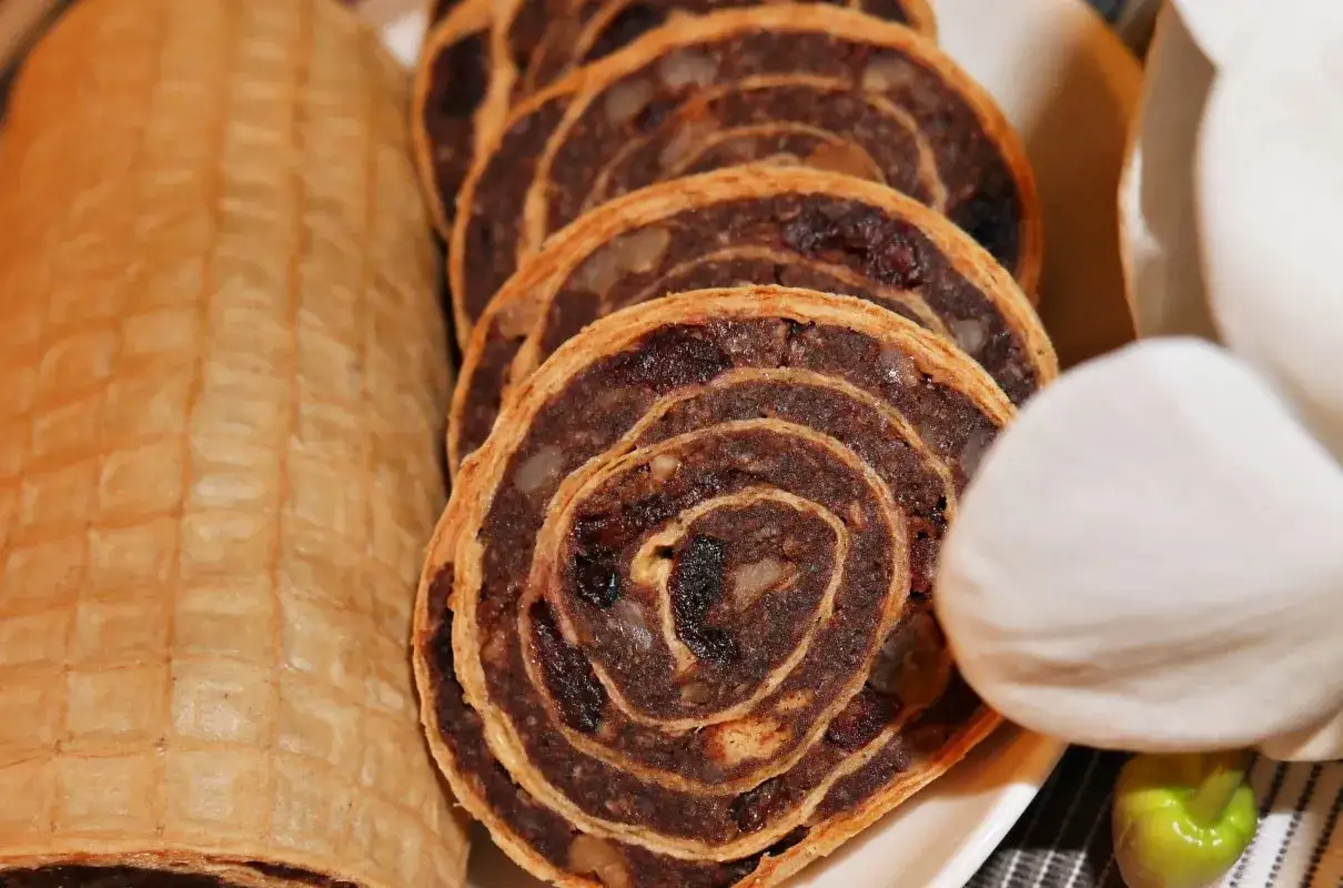 Rolada waflowa z galaretką, pokrojona w plastry, ukazuje ciemne nadzienie z bakaliami. Obok leży cała rolada w waflach.