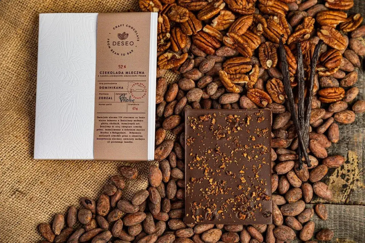 Czekolada mleczna 52% z orzechami pekan i wanilią. Całość odzwierciedla proces bean to bar, od ziaren kakao po gotowy produkt.