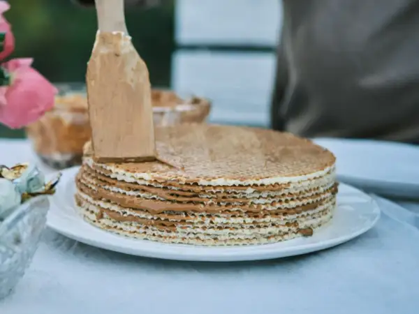 Nakładanie kremu na ciasto na gofrach bez pieczenia. Warstwy wafli przełożone pysznym, karmelowym nadzieniem.